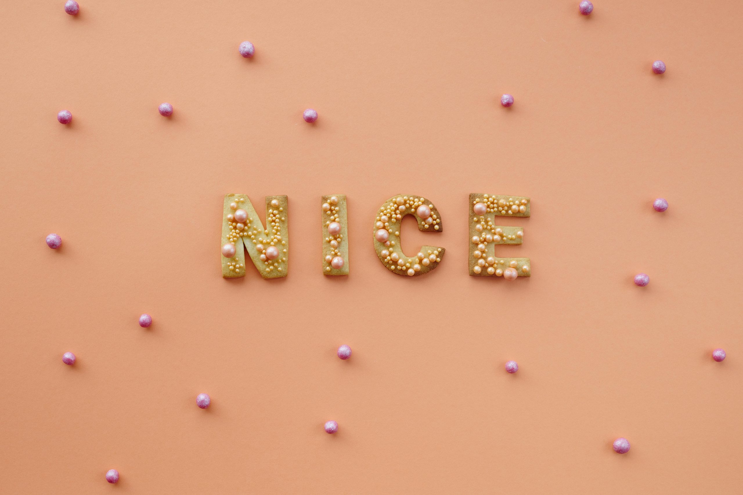 Flat lay of 'NICE' cookies with sprinkles on orange background. Fun and creative food art.